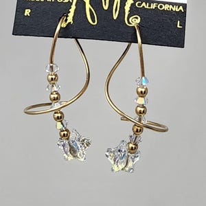 May include: Gold tone earrings with a spiral design and clear crystal beads. The earrings are on a black card with the text "HARRY MASON CALIFORNIA" printed on it.