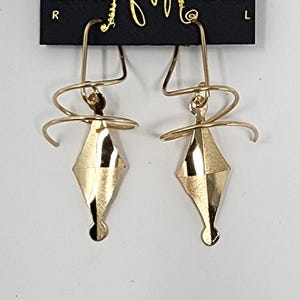 May include: Gold-toned earrings with a diamond-shaped pendant and a twisted wire design. The earrings are on a black card with the text "HARRY MASON" and "Made in USA CALIFORNIA".