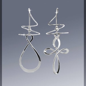May include: A pair of silver dangle earrings with a unique, abstract design. The earrings are made of thin, twisted wire that forms a loop at the bottom. The top of the earrings features a small, round bead.