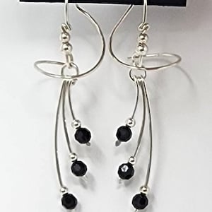 May include: Silver dangle earrings with black beads and a curved wire design. The earrings are on a card that says "Harry Mason California".