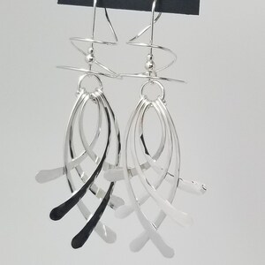 May include: Silver dangle earrings with a spiral design at the top and multiple curved silver strands hanging down. The earrings are on a card that says "Harry Mason Designer Jewelry" and "Made in USA California".