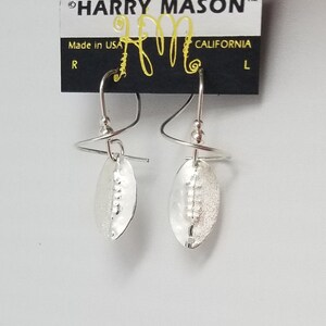 May include: Silver earrings with a hammered oval design and a twisted wire detail. The earrings are hanging from a card that says "HARRY MASON" and "CALIFORNIA".