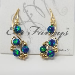 May include: A pair of gold earrings with blue and green opal beads. The earrings are shaped like a vine with a small loop at the top for hanging.