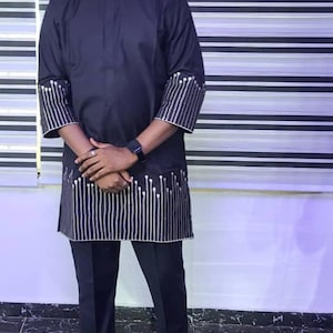 May include: A man wearing a black long-sleeved shirt with silver embroidery and black trousers. He is wearing brown leather shoes with gold buckles.