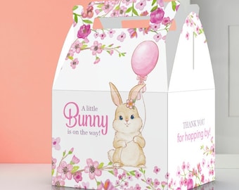 May include: A white favor box with a pink bunny holding a pink balloon. The box is decorated with pink flowers and the text "A little Bunny is on the way!" and "Thank you for hopping by!"