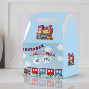 May include: A blue and red train-themed favor box with a handle. The box has a picture of a red train with yellow wheels and a blue smoke stack. The text on the box says "Chugga Chugga Two Two".