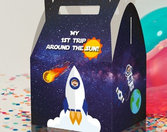 May include: A blue and black party favor box with a rocket ship, a comet, and a sun. The box says "My 1st Trip Around The Sun!"