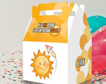May include: A yellow and white favor box with a sun and rocket design. The box has a handle and says "My 1st Trip Around The Sun!" and "ONE" on the front.