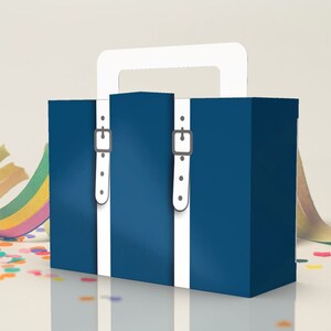 May include: A blue cardboard suitcase with white straps and a white handle. The suitcase is sitting on a white surface with confetti and a colorful streamer.