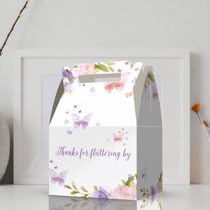 May include: A white favor box with a butterfly and floral design. The box has a handle and says "Thanks for fluttering by".