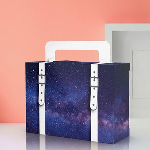 May include: A blue and white gift box with a galaxy print and white straps with silver buckles. The box has a handle on top.