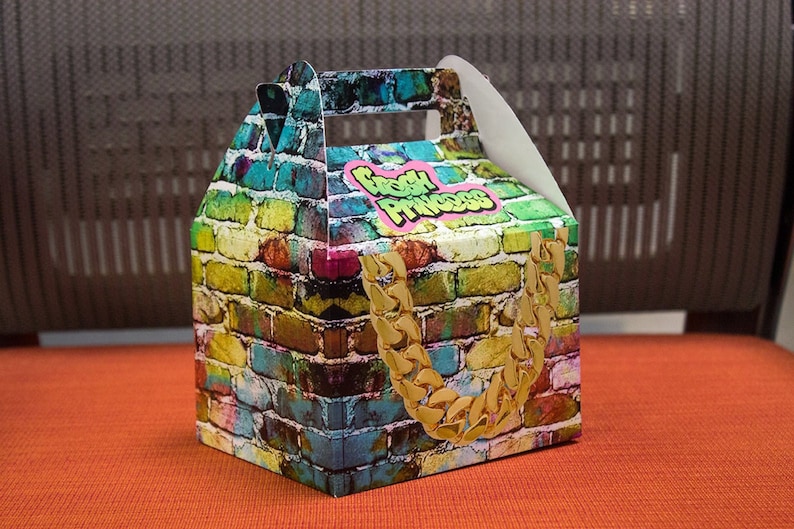Puede incluir: Una caja de cart&oacute;n colorida con un patr&oacute;n de ladrillo y un dise&ntilde;o de cadena dorada. La caja tiene un asa y dice "Fresh Princess" en la parte delantera.