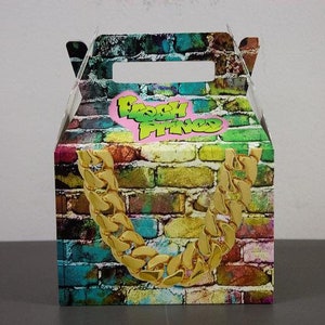 Puede incluir: Una caja de cart&oacute;n colorida para favores de fiesta con un patr&oacute;n de pared de ladrillo y un dise&ntilde;o de cadena dorada. La caja tiene un asa y dice "Fresh Prince" en letras verdes sobre un coraz&oacute;n rosa.