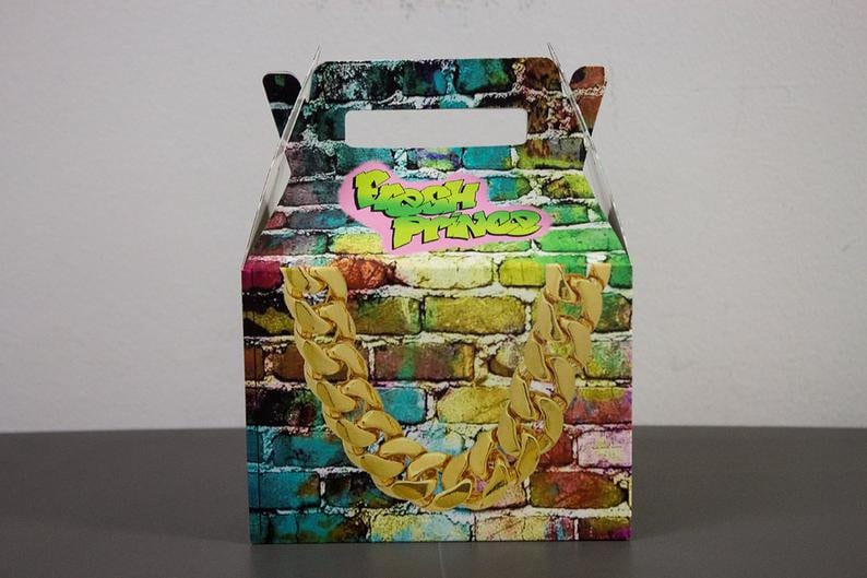Puede incluir: Una caja de cart&oacute;n colorida para favores de fiesta con un patr&oacute;n de pared de ladrillo y un dise&ntilde;o de cadena dorada. La caja tiene un asa y dice "Fresh Prince" en letras verdes sobre un coraz&oacute;n rosa.