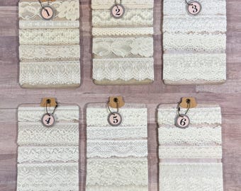 May include: Six displays of various ivory and white lace ribbons. Each display has a wooden backing, a metal chain, and a numbered tag. The lace designs include floral, geometric, and scalloped edges. The displays are arranged on a light wood surface.