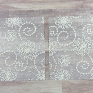 May include: Two pieces of white sheer fabric with an embroidered floral pattern. The fabric is translucent and the embroidery is delicate.