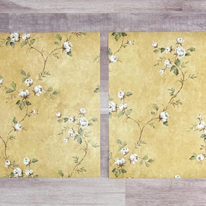 May include: Two sheets of yellow wallpaper with a white floral pattern. The wallpaper features a repeating pattern of small white flowers and green leaves on a yellow background.