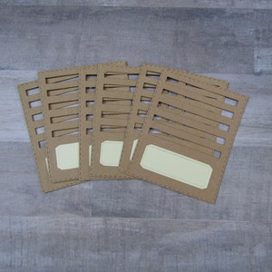 May include: Six brown cardstock gift tags with a decorative cut-out design and a blank label. The tags have a stitched border.