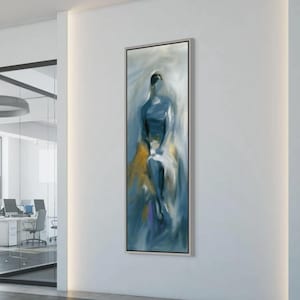 May include: Abstract painting in a silver frame. The artwork features a figure rendered in shades of blue, with accents of yellow and purple. The painting is displayed on a white wall in a modern office setting.
