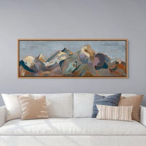 May include: A panoramic landscape painting in a light wood frame featuring stylized mountain peaks rendered in shades of blue, gray, gold, and rust. The artwork displays visible brushstrokes and abstract geometric shapes depicting a rugged mountain range.