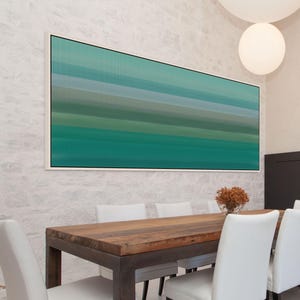 May include: A large, rectangular abstract artwork in shades of teal, green, and blue hangs on a white brick wall. The artwork is framed in white and features vertical lines creating a textured effect. Below, a wooden dining table with white chairs is set.