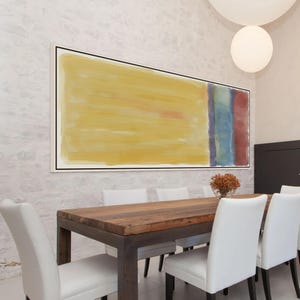 May include: Large abstract painting with a yellow background and a vertical stripe of blue, red, and green. The artwork is framed in black and hangs above a wooden dining table with white chairs. The room has a modern aesthetic.