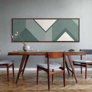 May include: A dining room scene featuring a wooden table and chairs. Above the table hangs a large rectangular artwork with a geometric design in shades of green and white. The chairs have gray striped seats and wooden frames, complementing the table's warm tones.