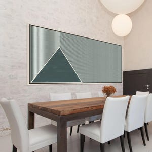 May include: Geometric abstract wall art in a white frame. The artwork features a teal triangle and striped sections in teal and white. The piece hangs above a wooden dining table with white chairs.