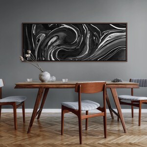 May include: A dining room scene featuring a mid-century modern wooden table and chairs. Above the table hangs a large abstract art piece with swirling black, white, and gray patterns. The room has a neutral color palette with a gray wall and a wooden floor.