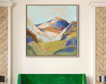 May include: Abstract landscape painting featuring a mountain range in shades of blue, orange, and green. The artwork is framed in a light wood frame and hangs above a green velvet sofa.