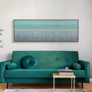 May include: Abstract artwork in a rectangular frame, with a gradient of blue and teal vertical lines. It hangs above a teal green velvet sofa with matching round and cylindrical cushions, and a small gold side table.