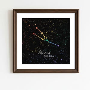 Puede incluir: Una impresión enmarcada que presenta la constelación de Tauro en un diseño colorido de arcoíris sobre un fondo negro estrellado. El texto "Taurus The Bull" está escrito en blanco debajo de la constelación.