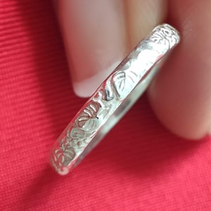 Puede incluir: Un anillo de plata con un diseño floral. El anillo es fino y delicado, y las flores están grabadas en el metal.