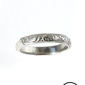 May include: A silver band ring with an intricate floral design.