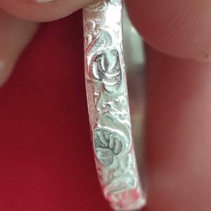 May include: Close-up of a silver ring with a floral design. The ring is smooth and shiny.