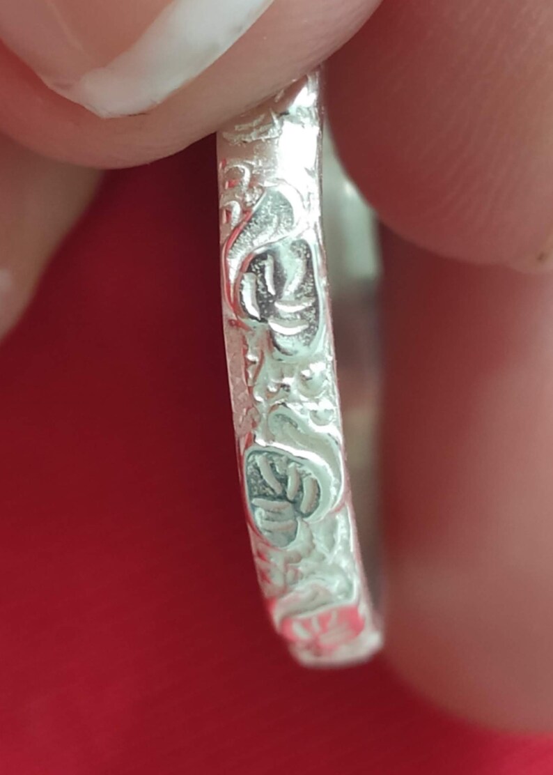 May include: Close-up of a silver ring with a floral design. The ring is smooth and shiny.