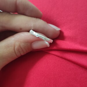 May include: A silver band ring with a floral design. The ring is thin and delicate.