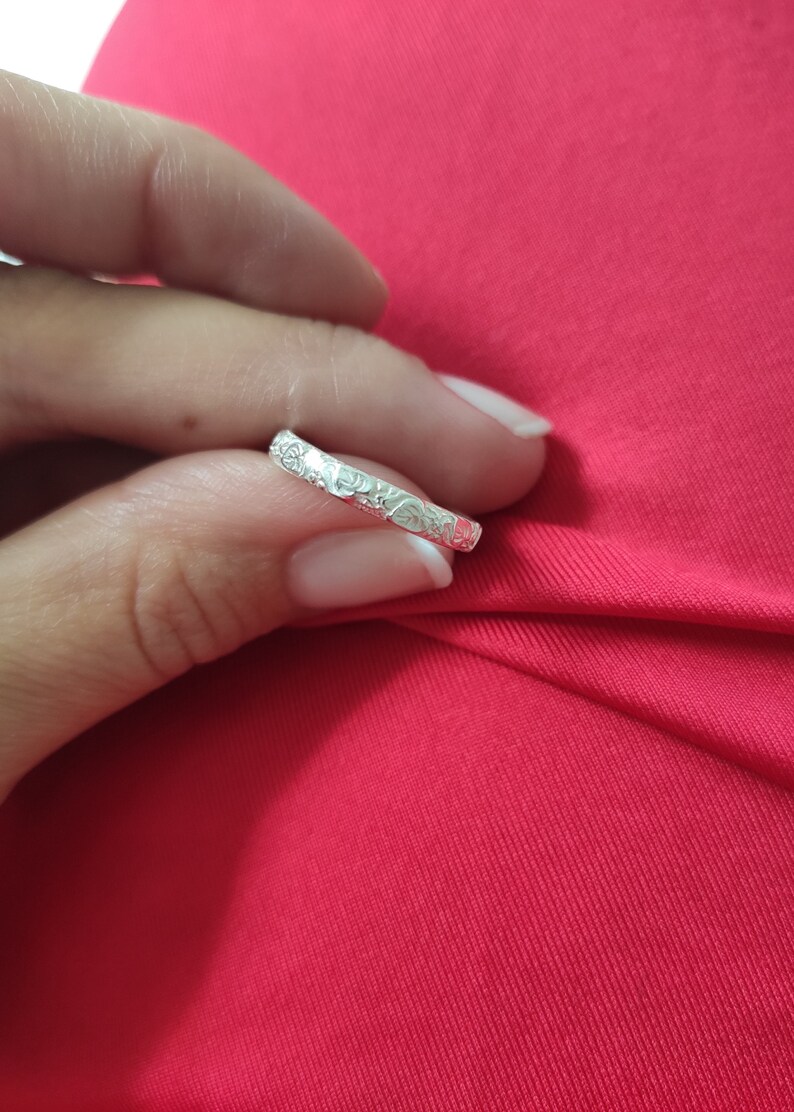 May include: A silver band ring with a floral design. The ring is thin and delicate.