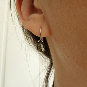 May include: A pair of silver dangle earrings with a pear-shaped green gemstone.