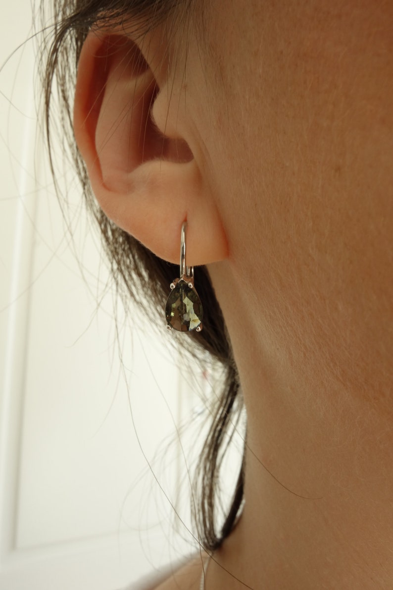 May include: A pair of silver dangle earrings with a pear-shaped green gemstone.