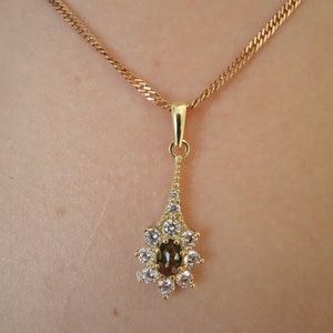 May include: A gold chain necklace with a pendant featuring a teardrop-shaped brown gemstone surrounded by smaller clear gemstones.