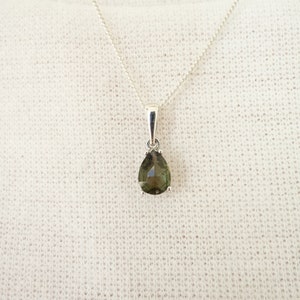 May include: A silver chain necklace with a pear-shaped green gemstone pendant.