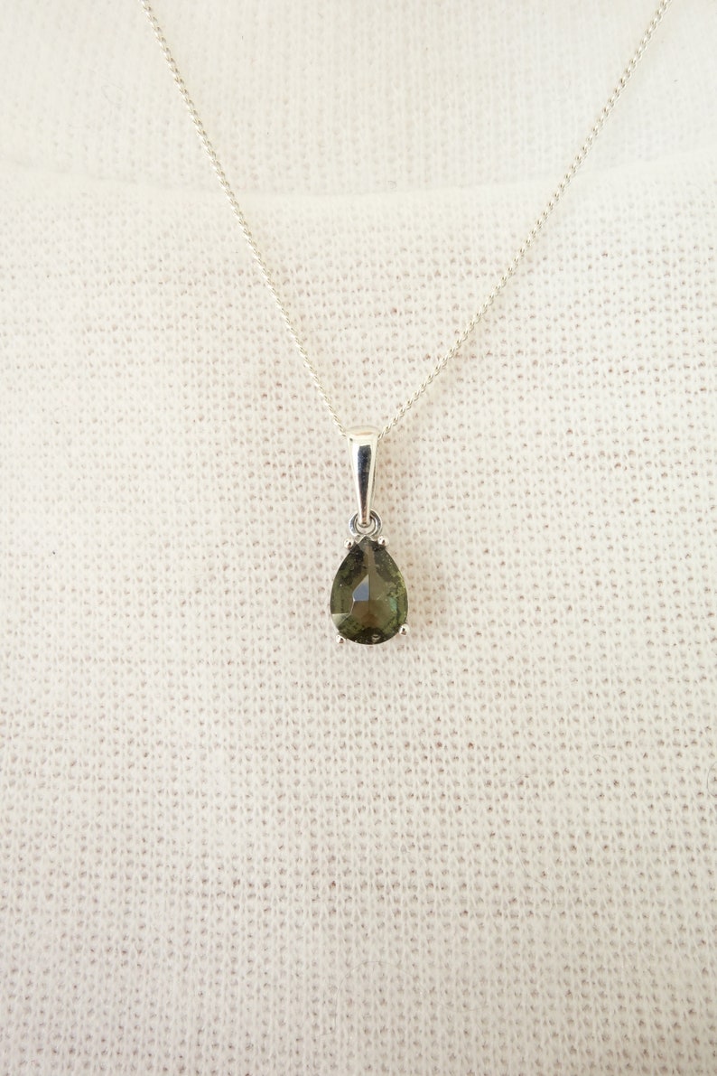 May include: A silver chain necklace with a pear-shaped green gemstone pendant.