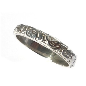 May include: A silver band ring with an intricate floral design.