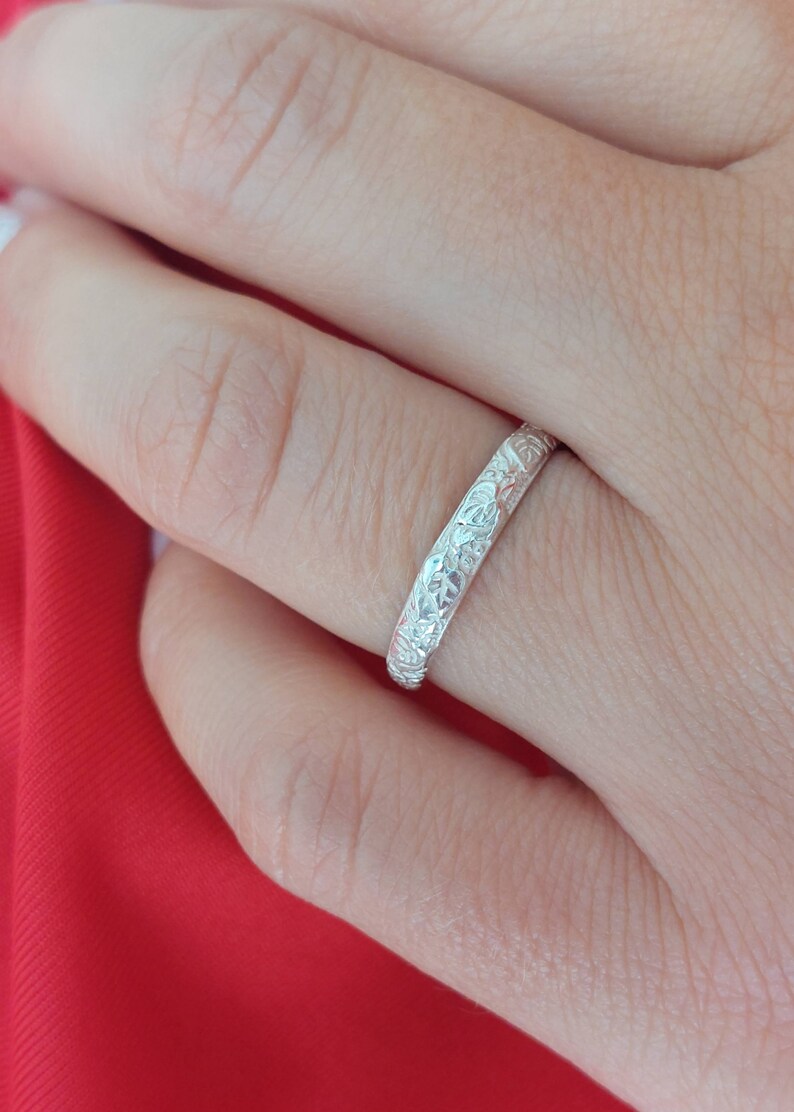 May include: A silver band ring with an intricate floral design. The ring is worn on a finger.