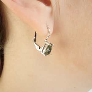 May include: Silver hoop earrings with a green gemstone. The earrings have a lever back closure.