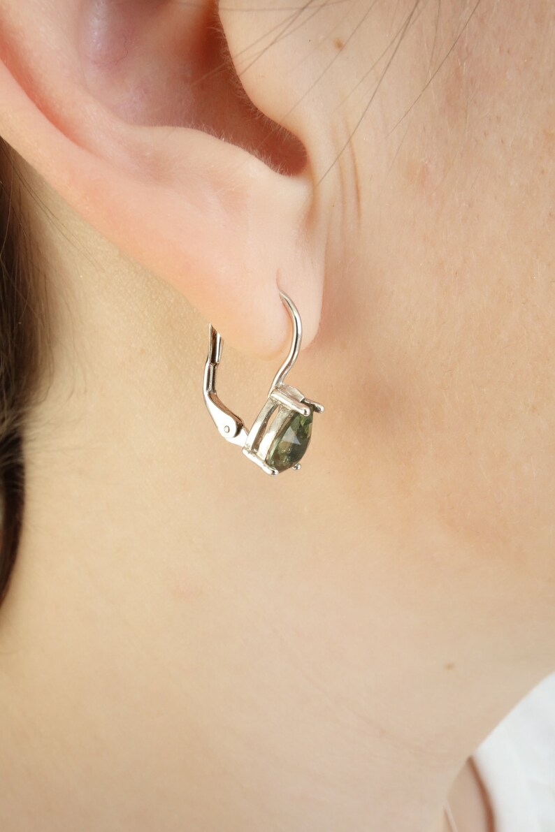 May include: Silver hoop earrings with a green gemstone. The earrings have a lever back closure.