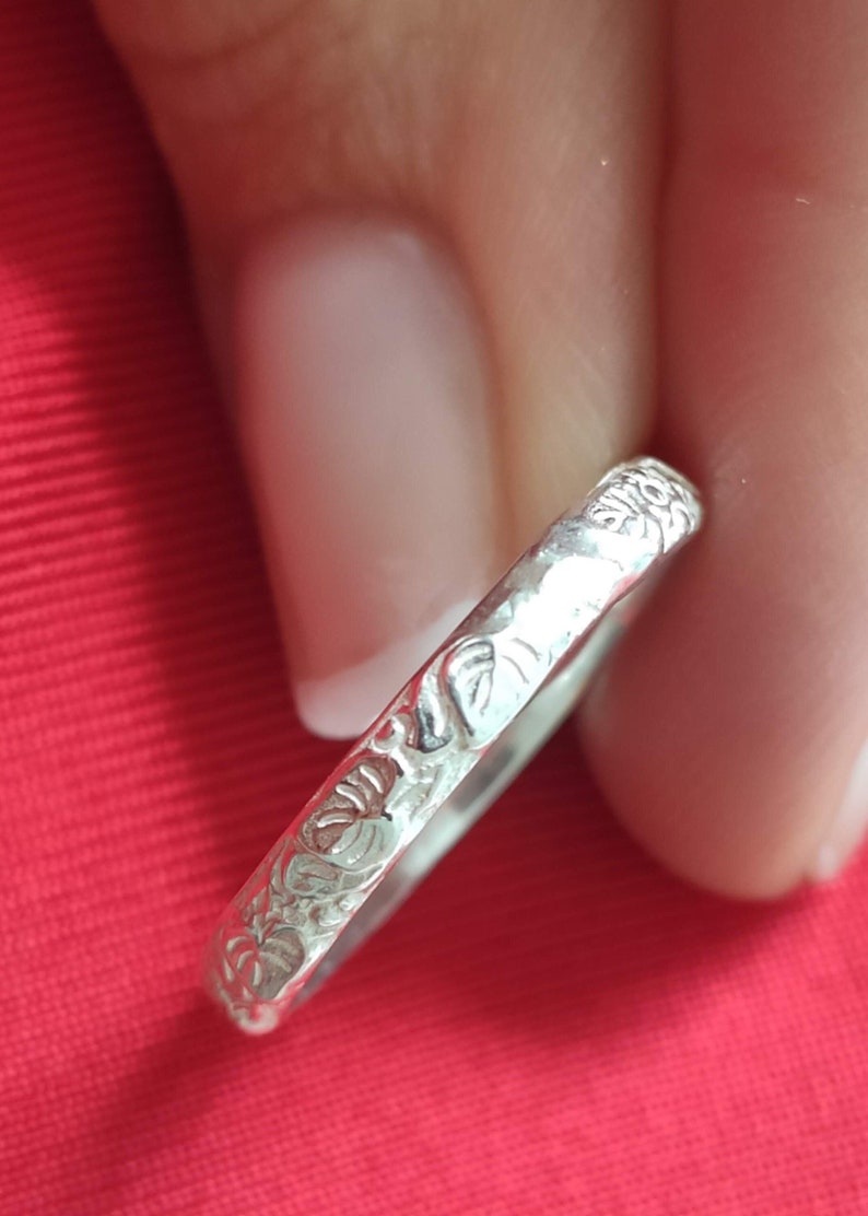 May include: A silver ring with a floral design. The ring is thin and delicate, and the flowers are etched into the metal.