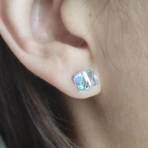 May include: A pair of iridescent blue square stud earrings. The earrings are small and have a simple design.