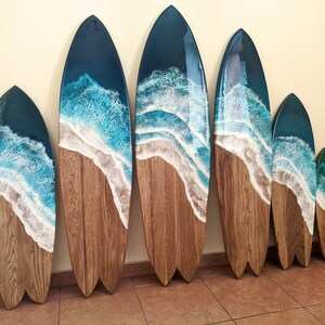 Op de afbeelding: Een set van zeven houten surfplank wanddecoraties met een blauw en wit hars ocean wave design. De surfplanken zijn gerangschikt in aflopende volgorde.